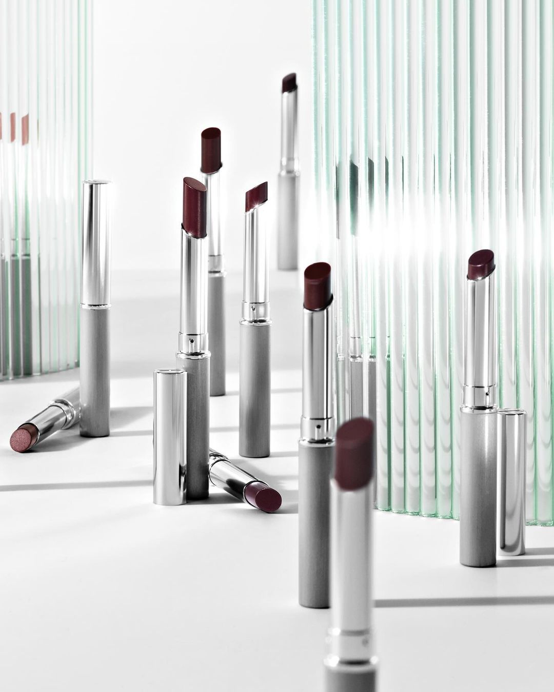 Elegant product shot of multiple silver lipstick tubes with burgundy tips, arranged on a white surface with translucent striped partitions.