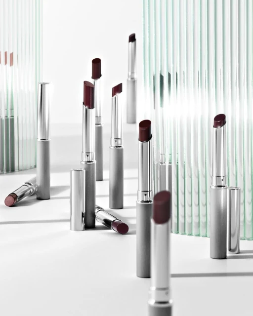 Elegant product shot of multiple silver lipstick tubes with burgundy tips, arranged on a white surface with translucent striped partitions.