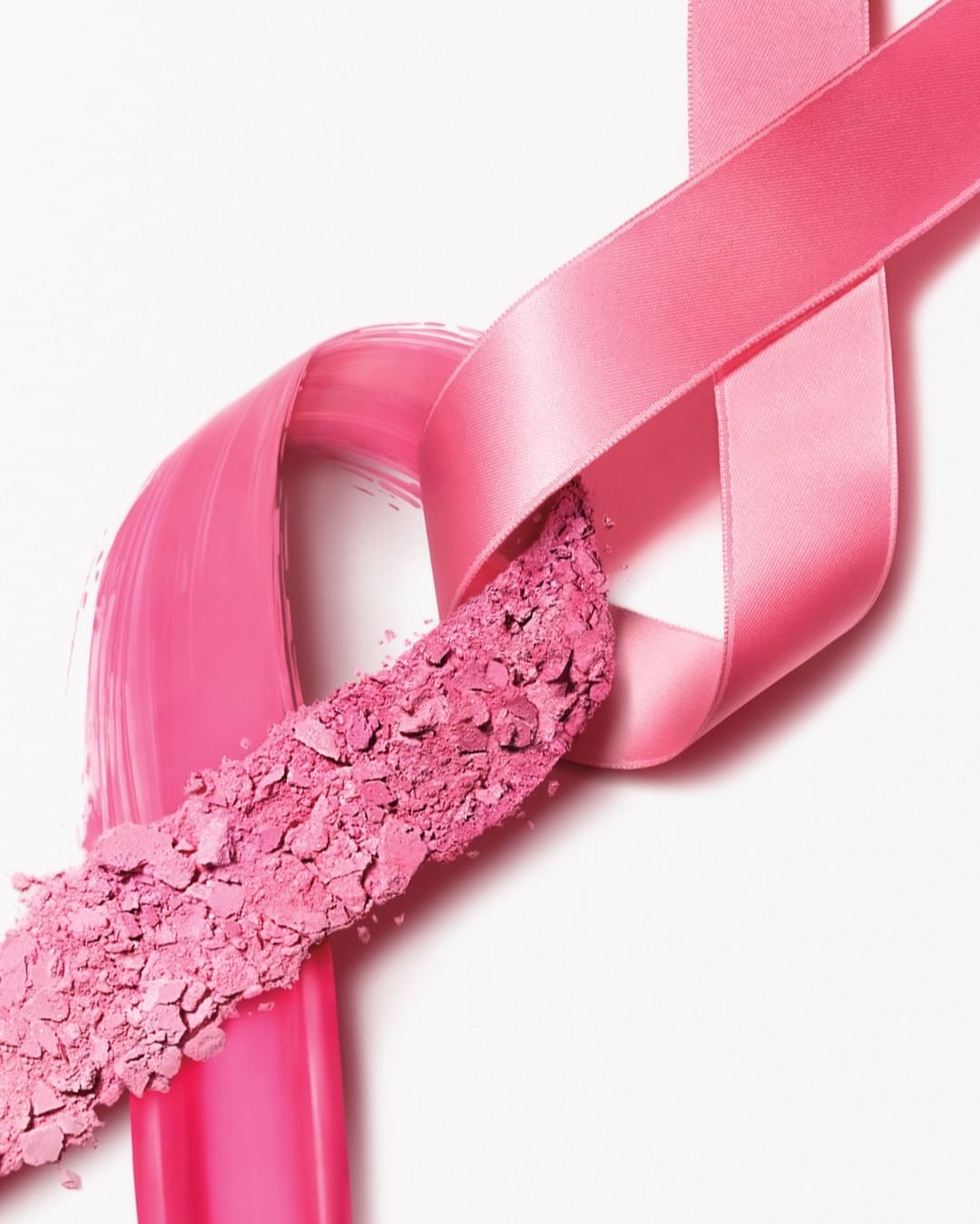 Pink ribbon tied in a knot, connecting a makeup brush stroke to loose pink cosmetic powder on a white background for beauty campaign.