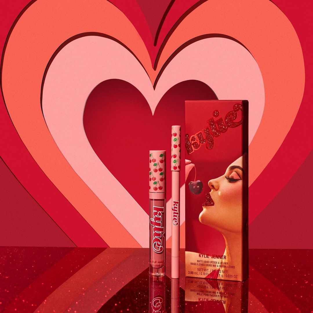 Kylie Cosmetics cherry-themed makeup set featuring lipstick, lip liner, and a packaging image of Kylie Jenner, set against heart backdrop.