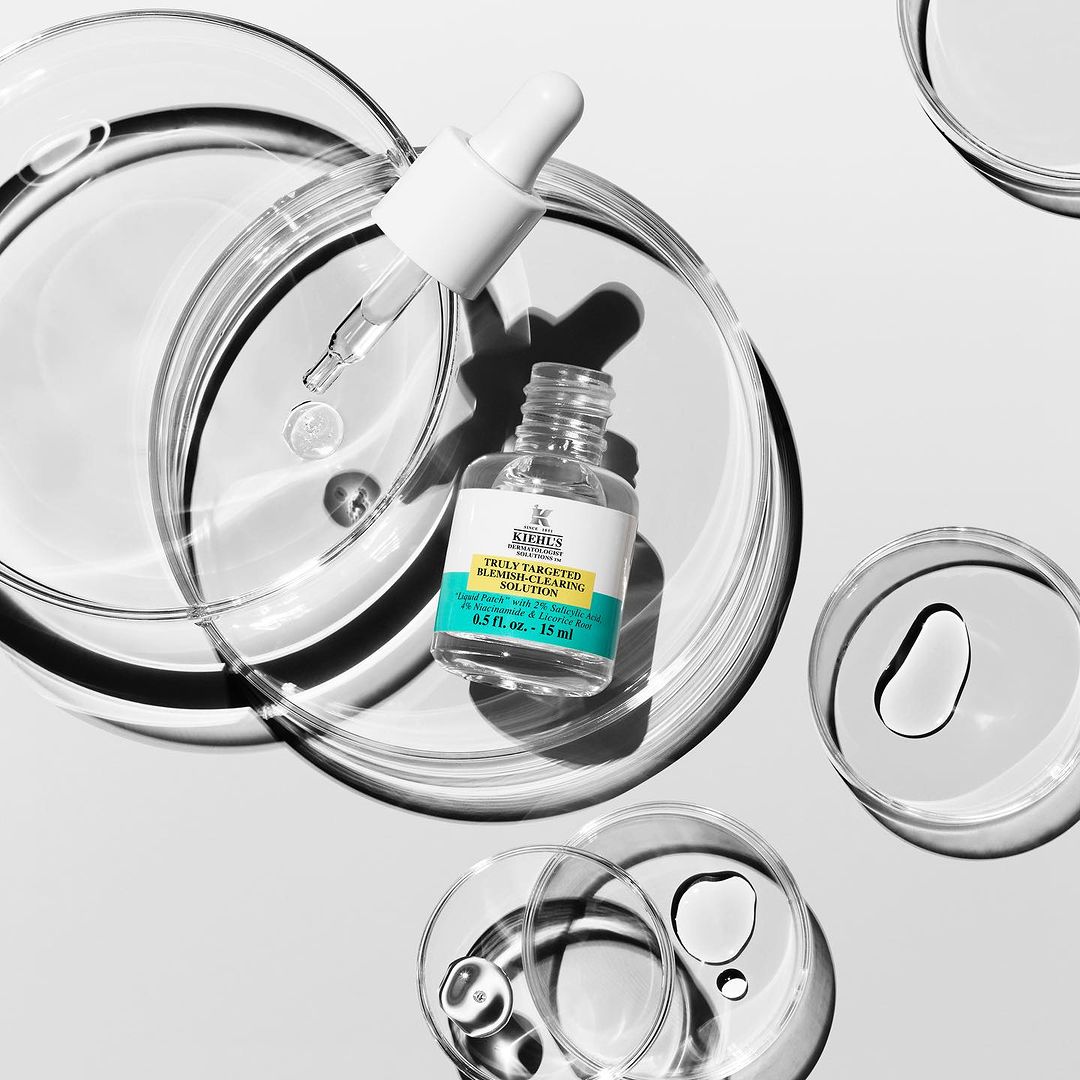 Kiehl's blemish treatment bottle with dropper on a petri dish. Skin care solution product shot, beauty industry, clean aesthetic, product photography.