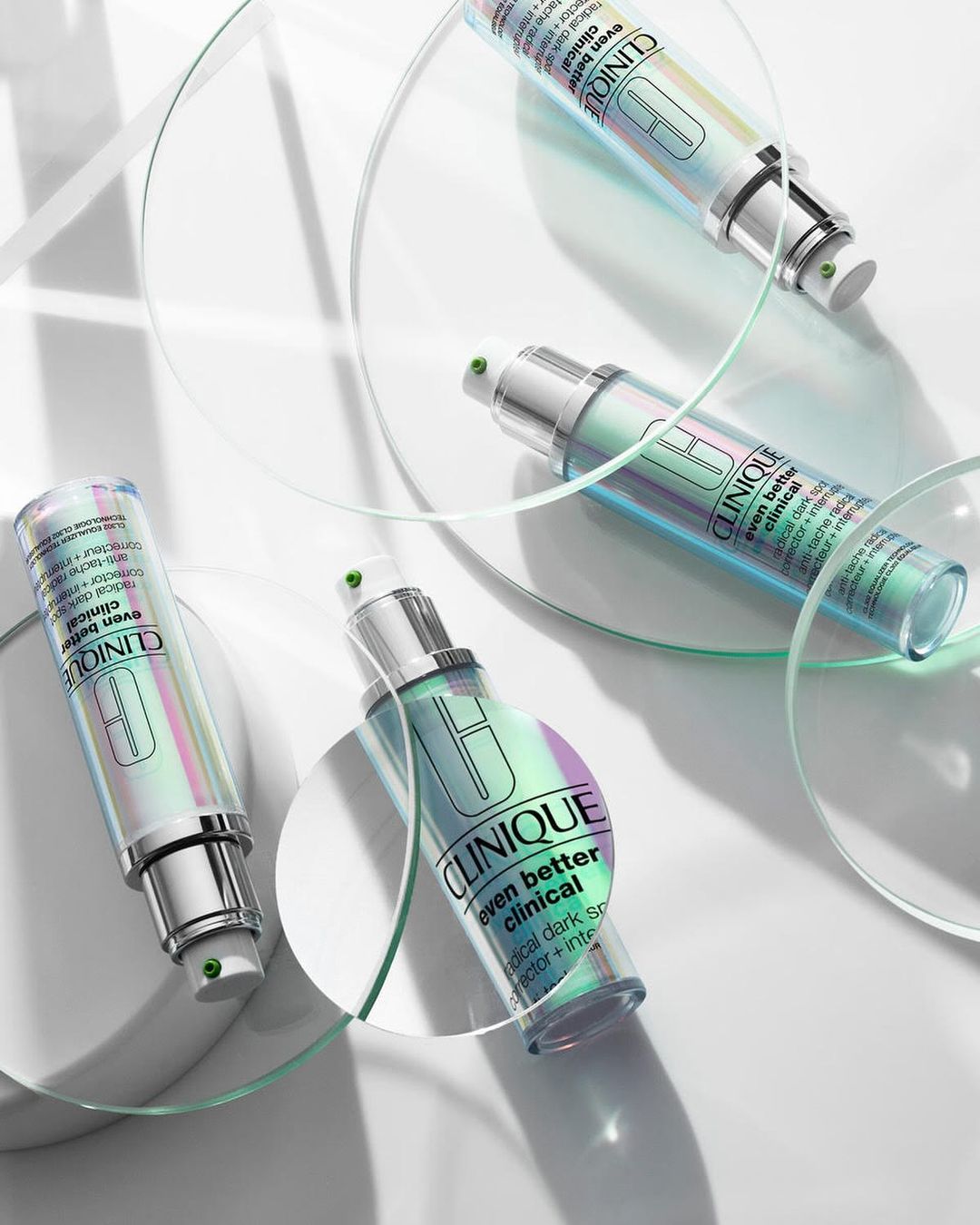 Clinique 'Even Better Clinical' serum bottles arranged with transparent circular stands on a white background in a beauty product shot.