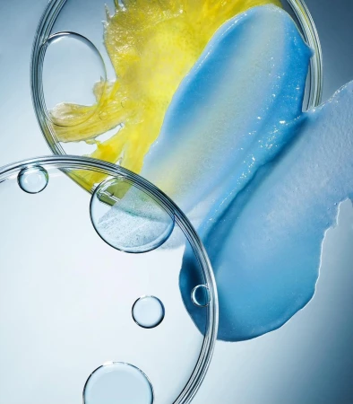 Macro shot of blue and yellow cosmetic cream smears in petri dishes, creating a textured, vibrant skincare product presentation.