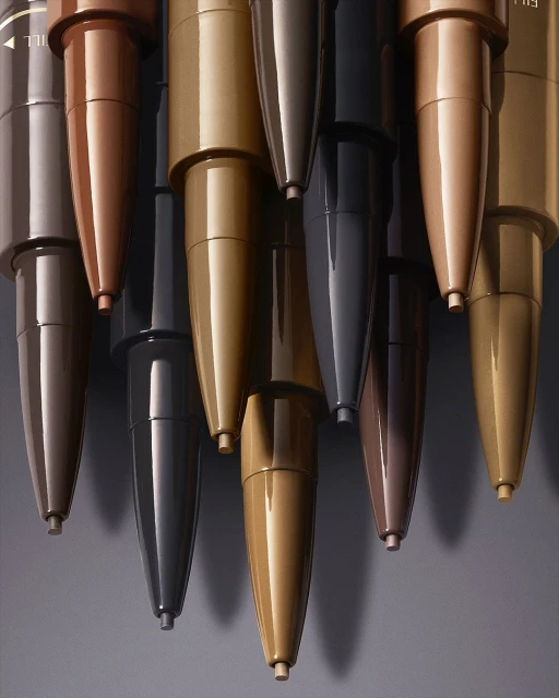 Close-up of multiple metallic-colored eyeliner pencils in brown, gold, and grey tones, neatly arranged in a row for a beauty-themed composition.