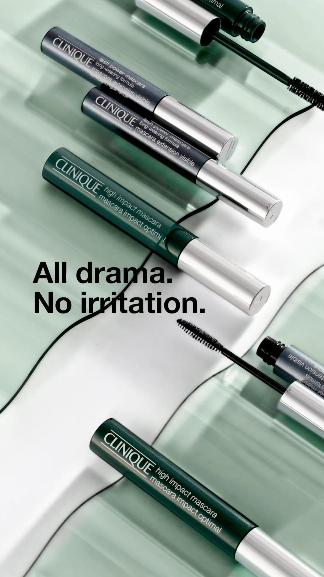 Close-up shot of Clinique high impact mascara tubes in green and silver on a light green patterned surface for a beauty product advertisement.