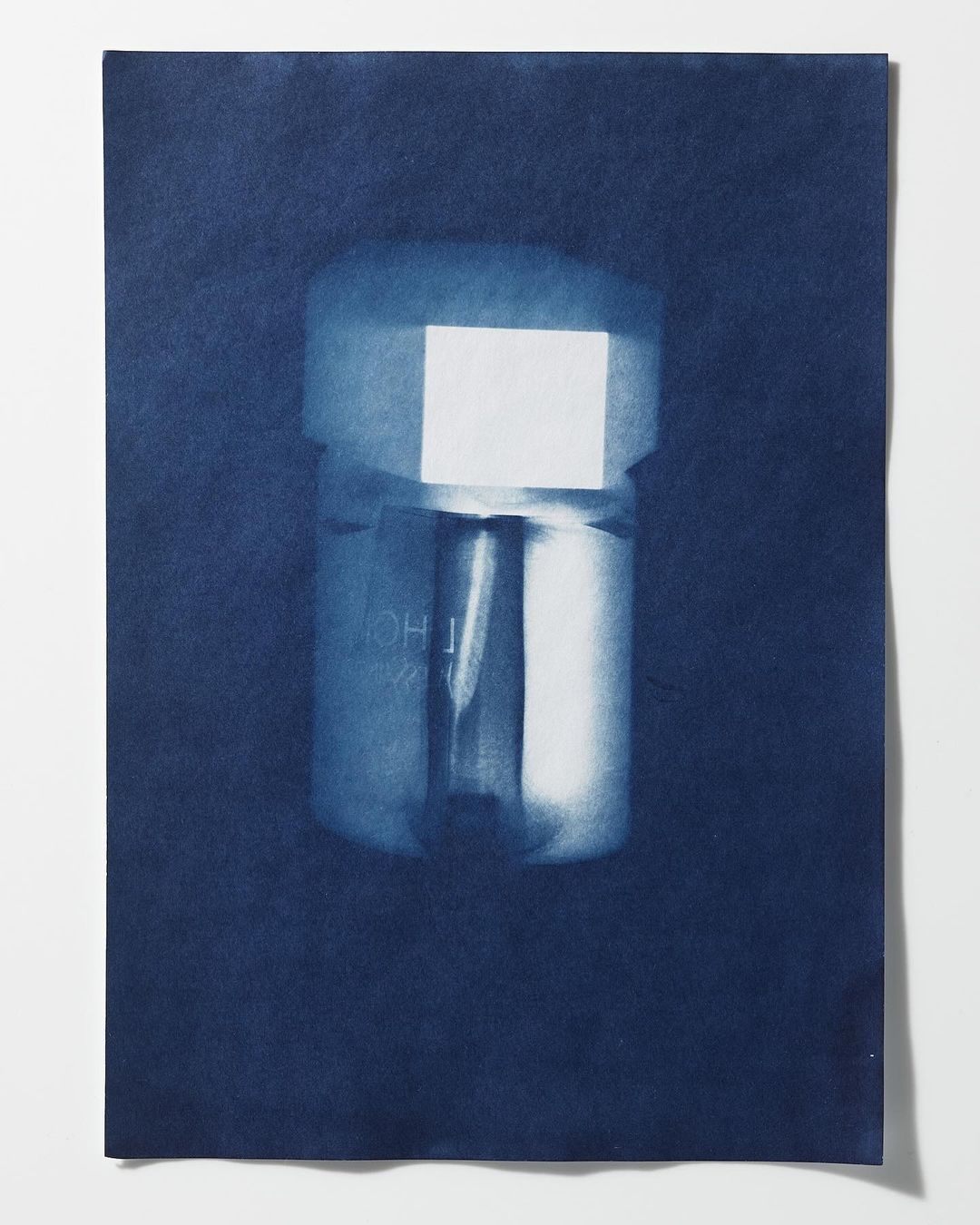 Cyanotype photograph of a metallic object, possibly a connector or fitting, set against a deep blue paper backdrop.