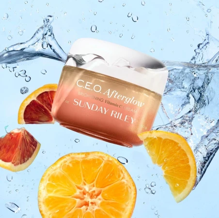 Bright C.E.O. Afterglow brightening Vitamin C cream by Sunday Riley with orange slices and water splashes against light blue background.