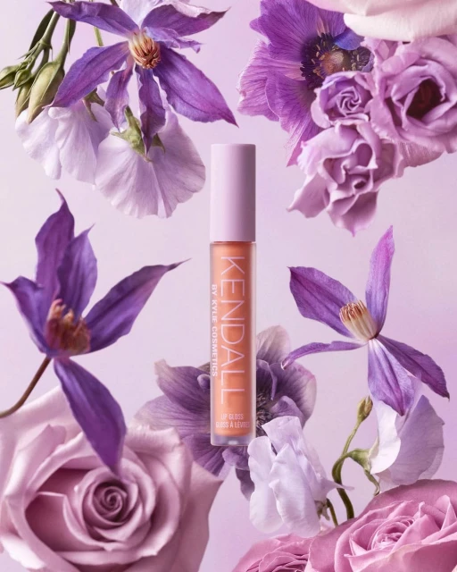 KENDALL by Kylie Cosmetics lip gloss product shot surrounded by lavender, purple, and white roses and other floral accents.