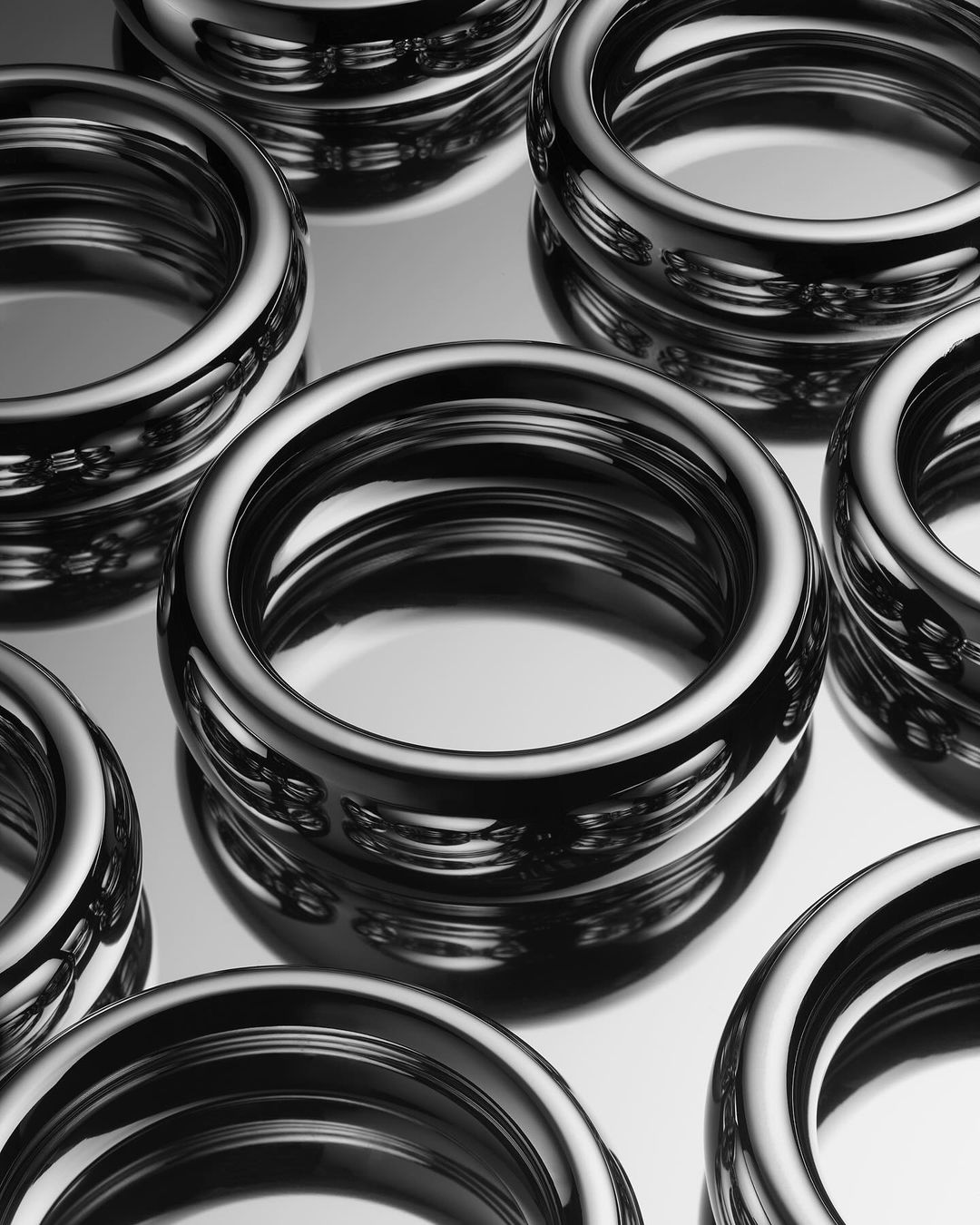 Shiny chrome metal rings arranged on a reflective surface with multiple rings stacked on top of each other in an indoor setting.