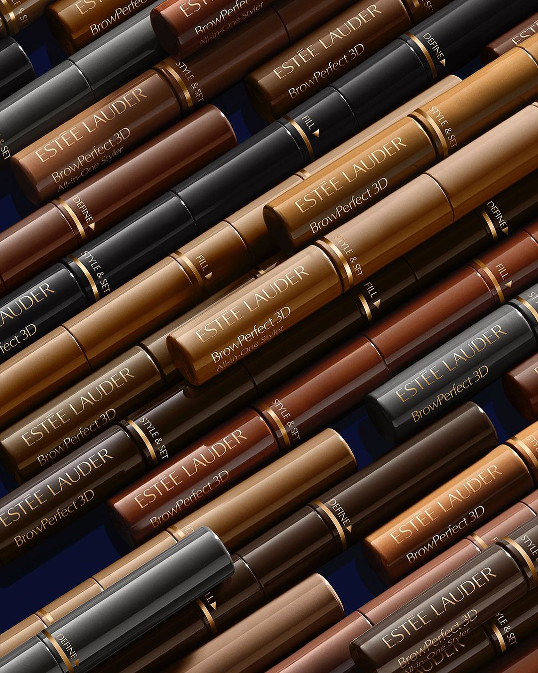 Multiple tubes of Estee Lauder Brow Perfect 3D brow gel in different shades arranged on a blue surface with gold lettering.