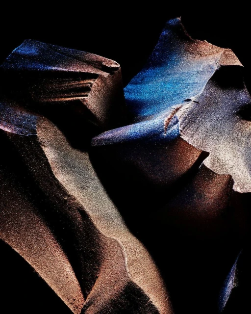 Abstract image featuring flowing, layered forms with a shimmering, iridescent texture in blue and gold tones against a dark background.