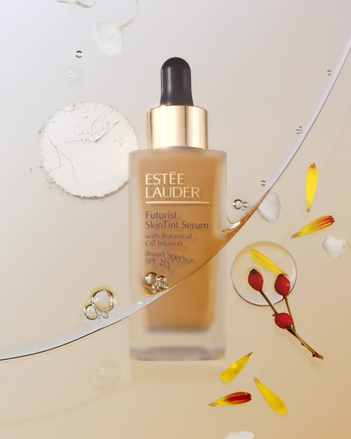 Estee Lauder Futurist SkinTint Serum in a square bottle with a dropper, surrounded by petals and powder on a light background.