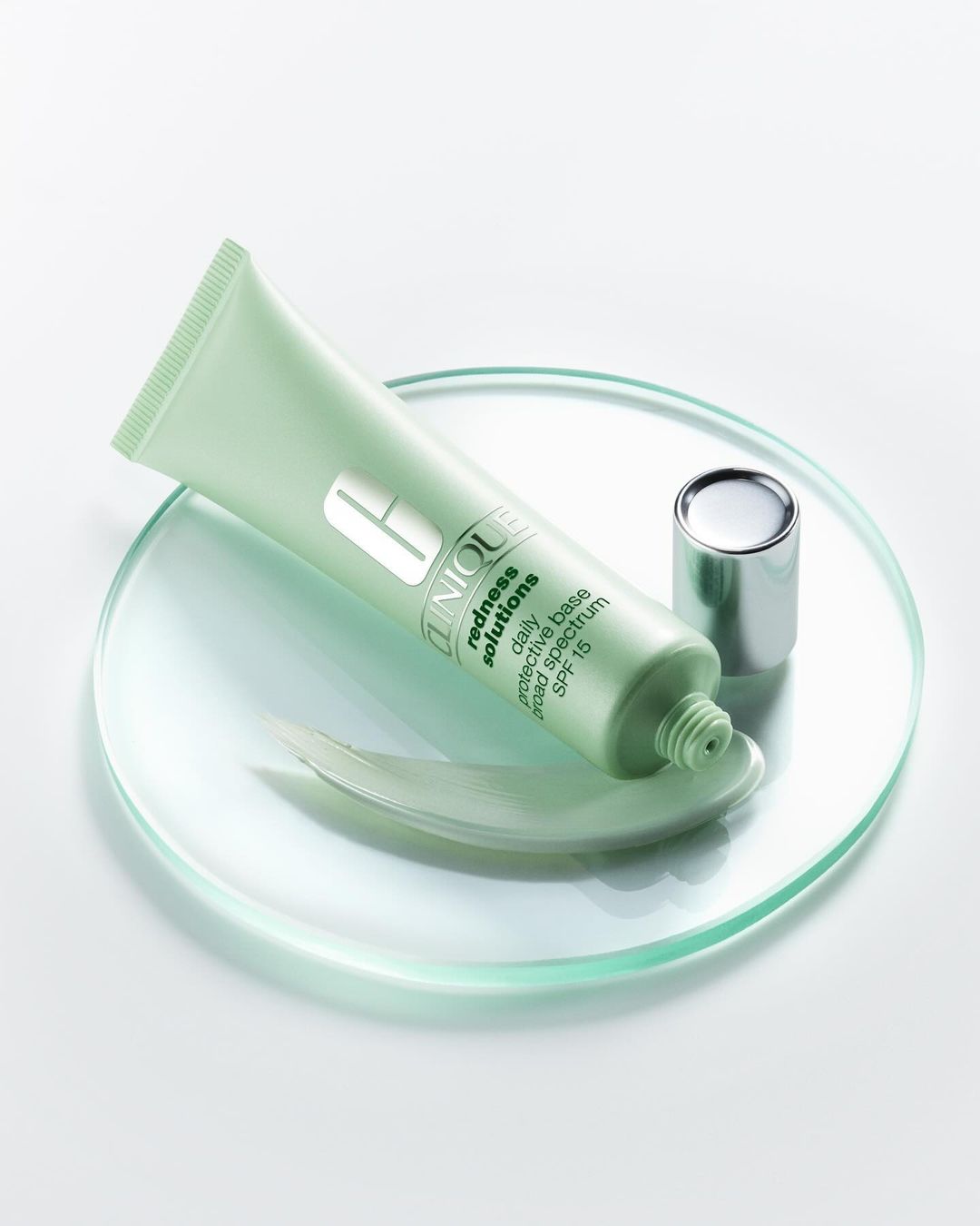 Product shot of Clinique Redness Solutions Daily Protective Base SPF 15 in a light green tube with a silver cap on a clear glass surface.