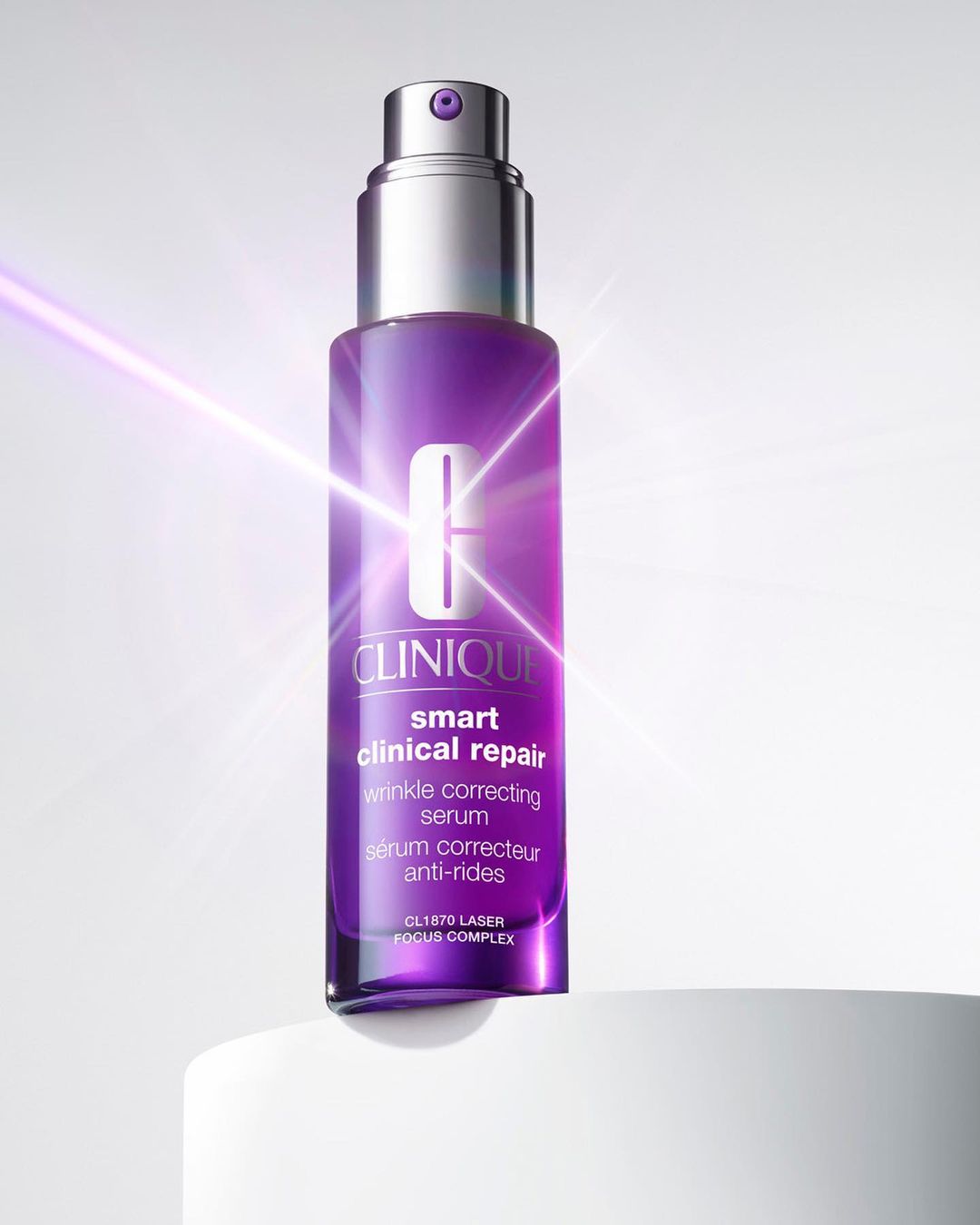 Clinique Smart Clinical Repair wrinkle correcting serum, packaged in a purple bottle with a silver top, sits on a white platform.