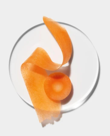 Close-up overhead shot of carrot peel and slice on clear plate against soft white background. Food and beverage still life.