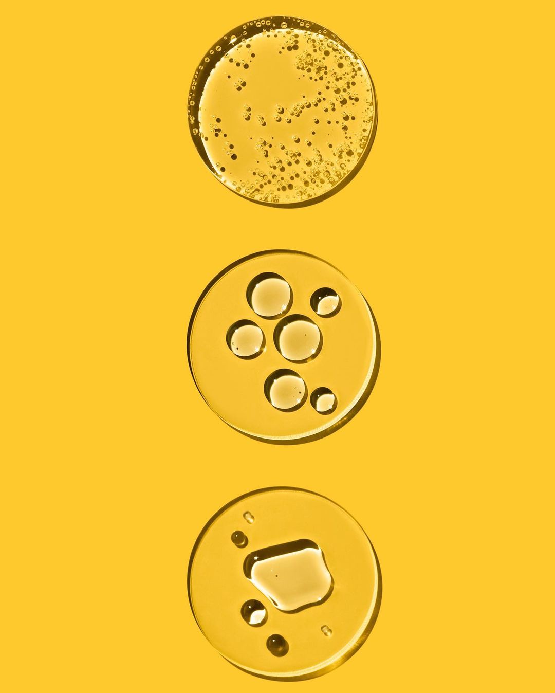 Three clear circles of liquid are arranged vertically on a bright yellow background, showing different oil-like textures and consistencies.