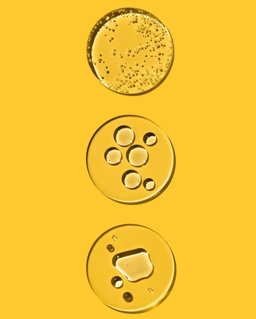 Three clear circles of liquid are arranged vertically on a bright yellow background, showing different oil-like textures and consistencies.