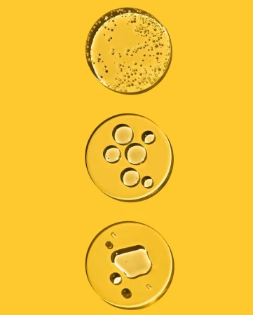 Three clear circles of liquid are arranged vertically on a bright yellow background, showing different oil-like textures and consistencies.