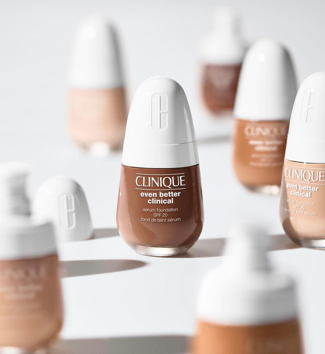 Clinique Even Better Clinical serum foundation bottles are displayed in a studio setting with a clean, minimalist aesthetic.