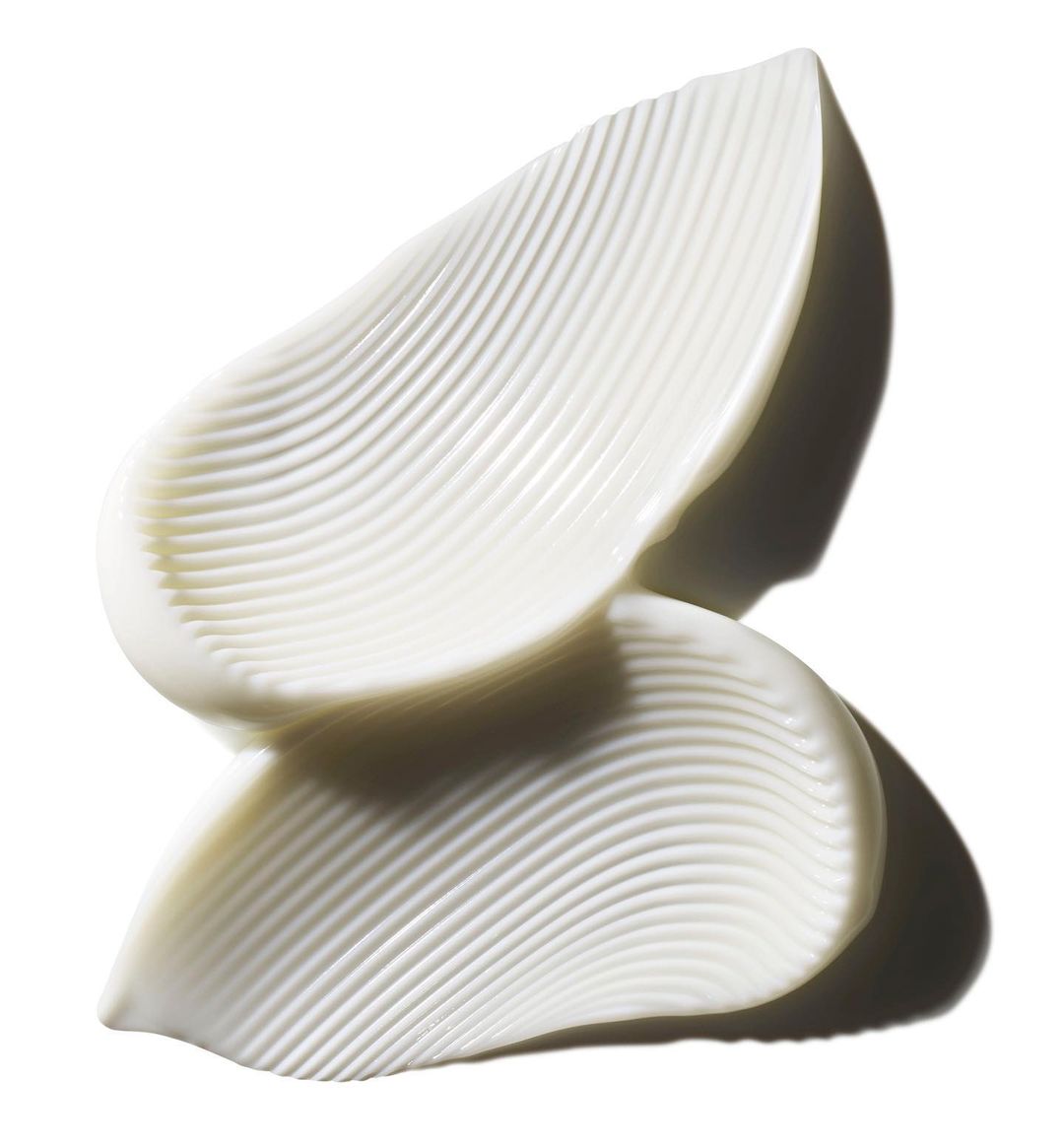 Close-up of thick, white cream swatches with a ribbed texture on a reflective surface against a bright, clean background.