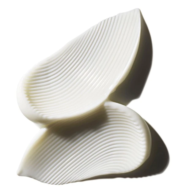 Close-up of thick, white cream swatches with a ribbed texture on a reflective surface against a bright, clean background.