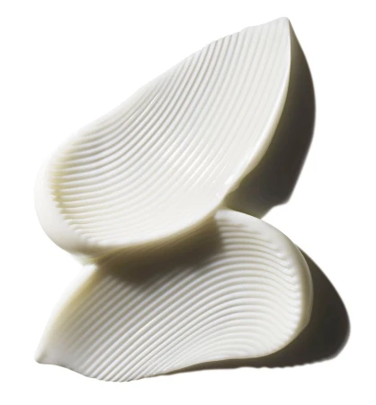 Close-up of thick, white cream swatches with a ribbed texture on a reflective surface against a bright, clean background.
