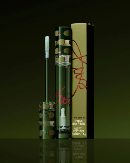 Kylie Cosmetics lip serum product shot. Cosmetic tube and box with olive pattern on a green surface, product photography.