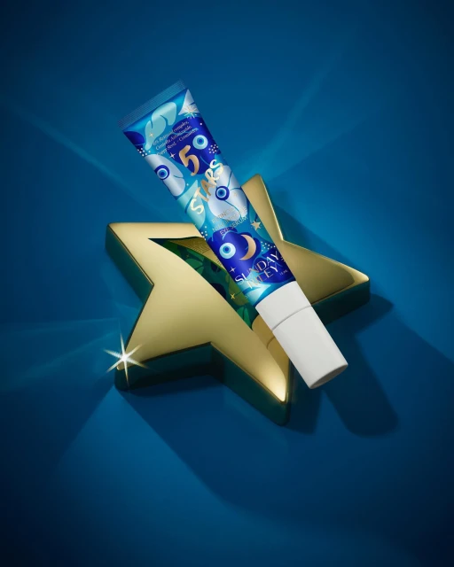 A tube of Sunday Riley beauty product is displayed on a gold star against a royal blue background, creating a luxurious and eye-catching presentation.
