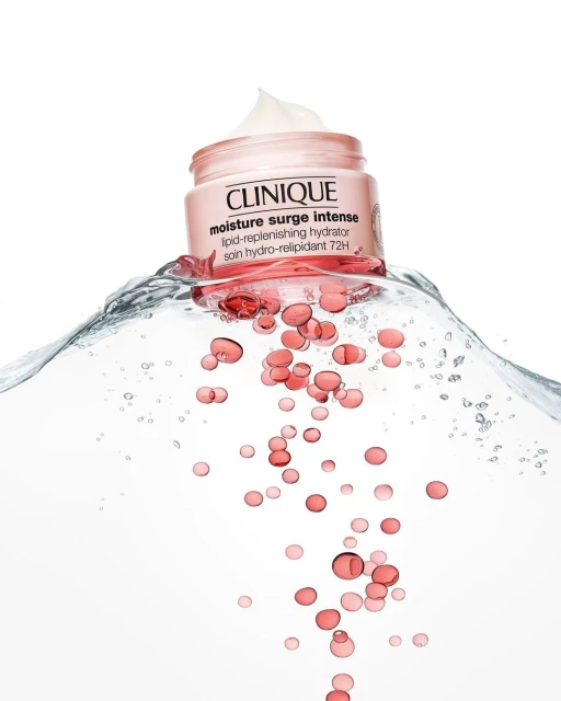 Clinique moisture surge intense cream jar shown in water with gel capsules on a white background, beauty and skincare product shot.