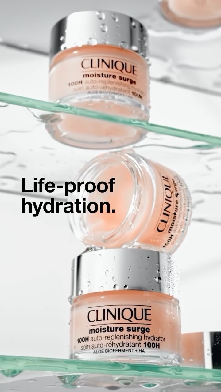 Three Clinique Moisture Surge hydrating skincare containers stacked on a reflective surface with visible water droplets, product shot.