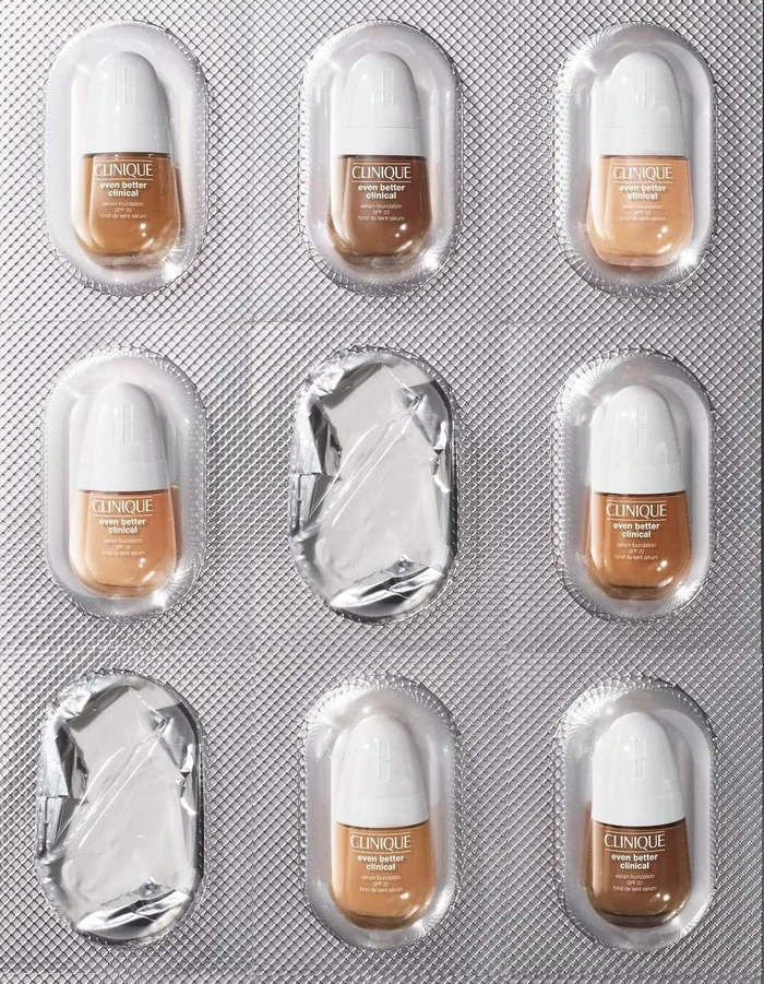 Clinique foundation bottles arranged like pills inside a blister pack on a metallic textured background