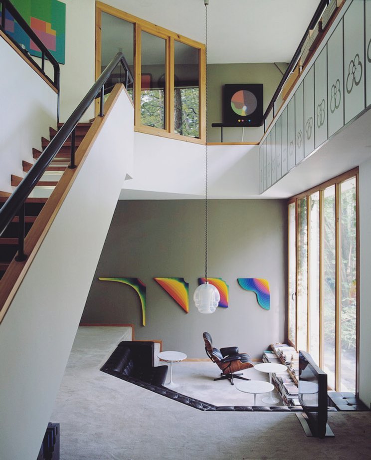 Interior view of a modern home features a staircase, a split-level living area with armchairs and round tables, and large windows.