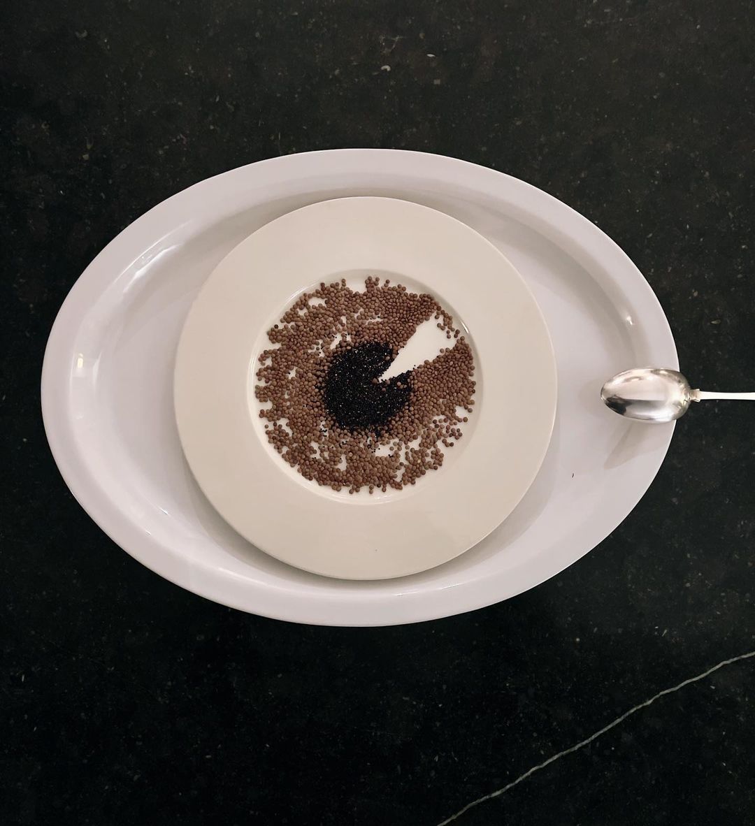 Overhead shot of a decorative plate featuring a brown and black eye design made of tiny spheres, resting on a large white plate.