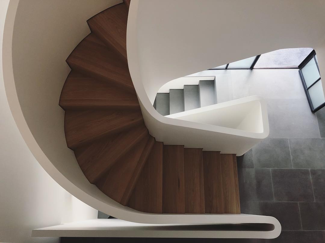 Spiral staircase with wood steps and white railing in modern home with natural light from a window. Interior architecture design.