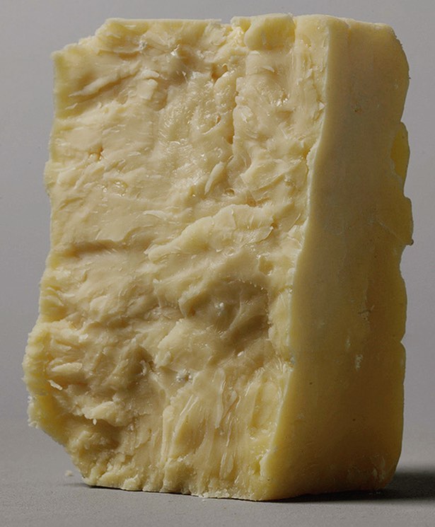 Close-up studio shot of a wedge of cheddar cheese featuring a rough, uneven texture, highlighted by a soft, neutral color palette.