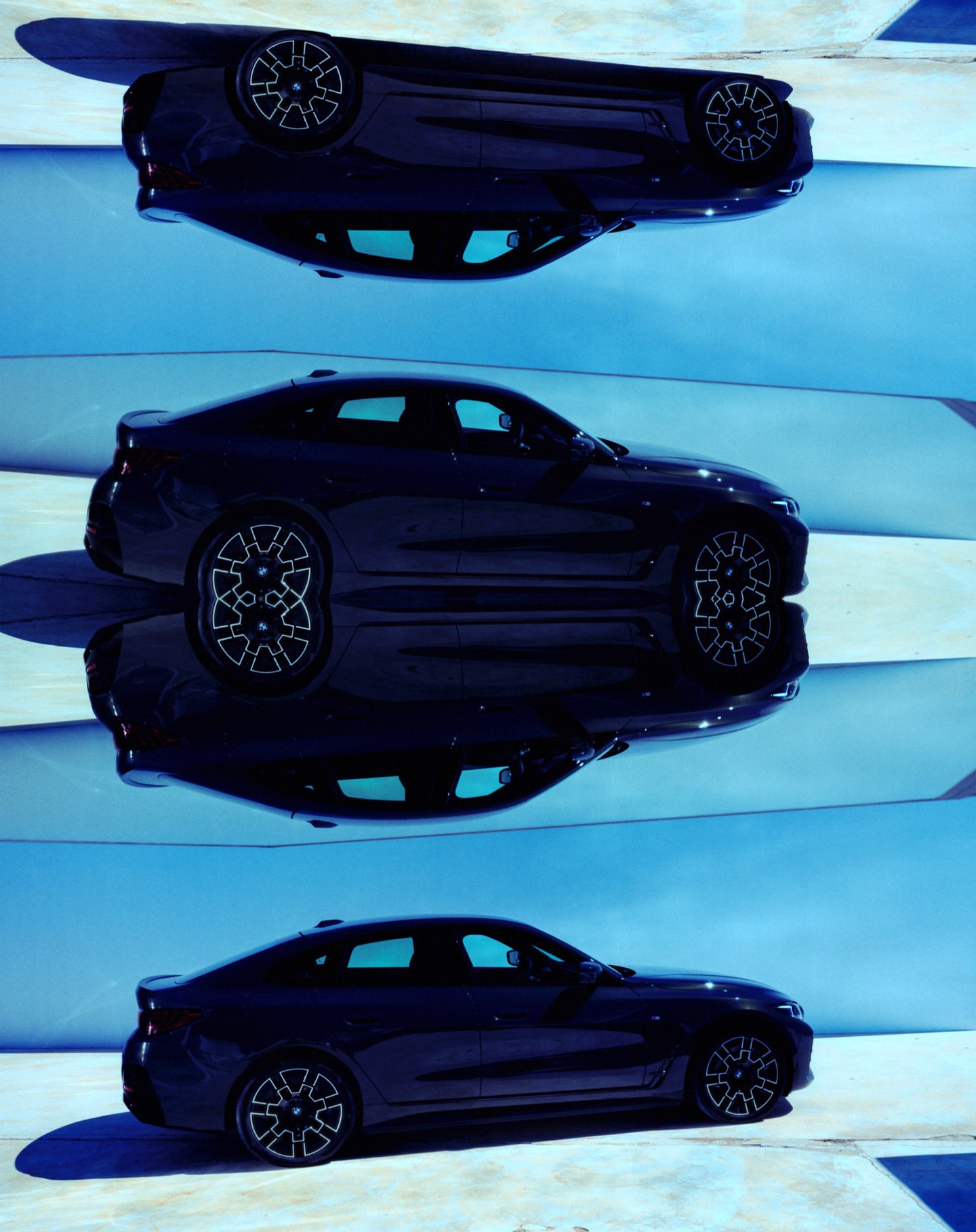 A black car is seen three times in a mirrored and repeating way on a glossy surface under a bright, blue sky on a sunny day.
