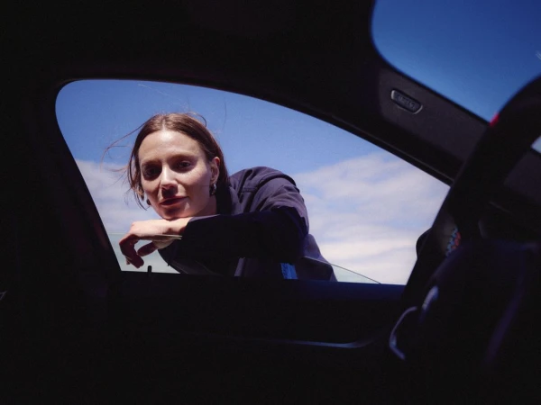 Woman leaning on car window looking into the vehicle against a bright blue sky captured by Matthew Jones.