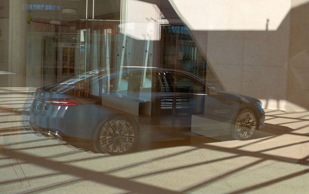 Dark blue sedan car parked in front of a modern building with glass windows, reflecting the urban scene in sunlight.