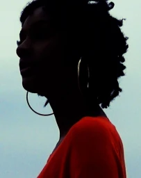 Profile silhouette of a woman wearing hoop earrings and an orange top against a pale sky background