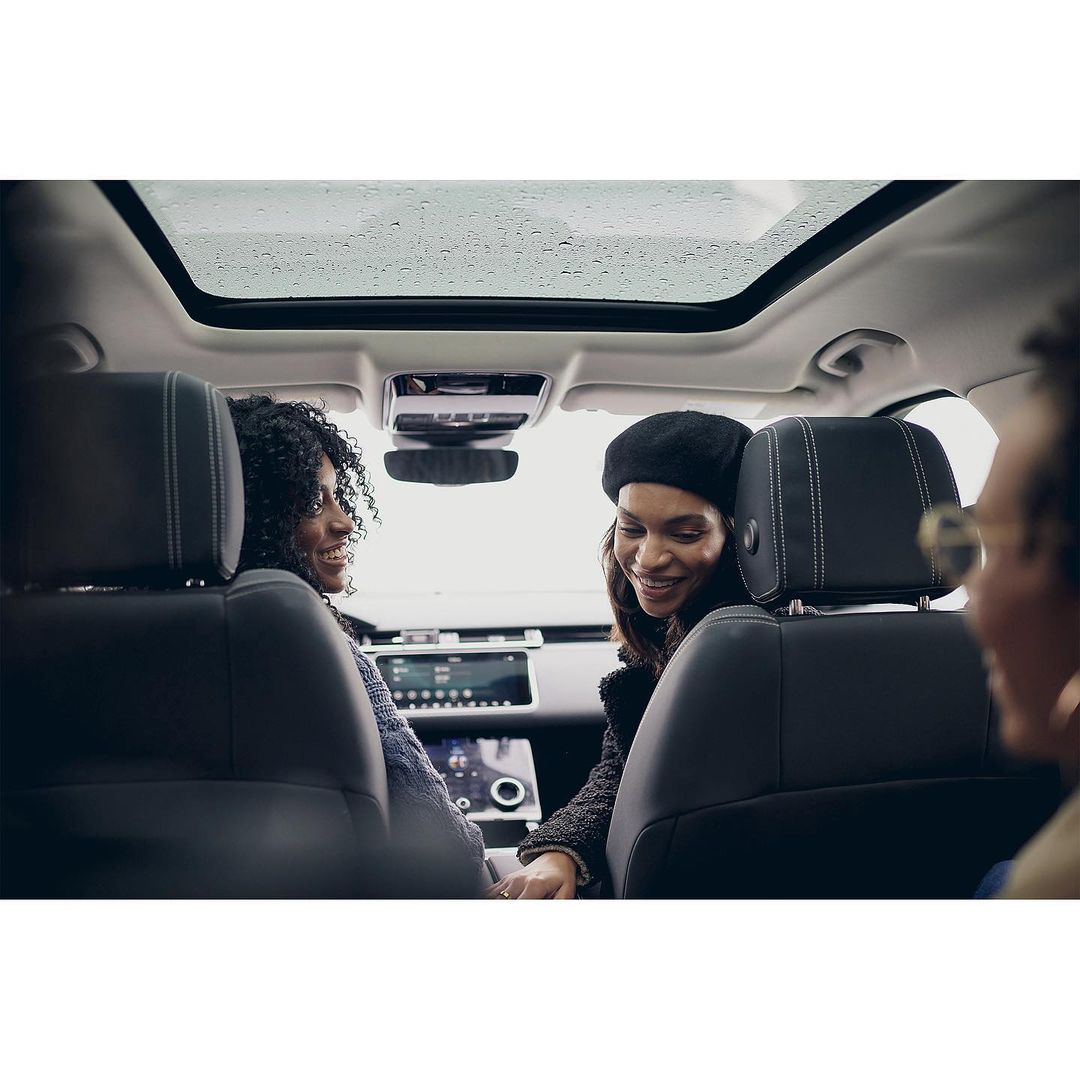 Two women inside a car with a sunroof. One woman is wearing a black beret, both are smiling, and the interior is modern.