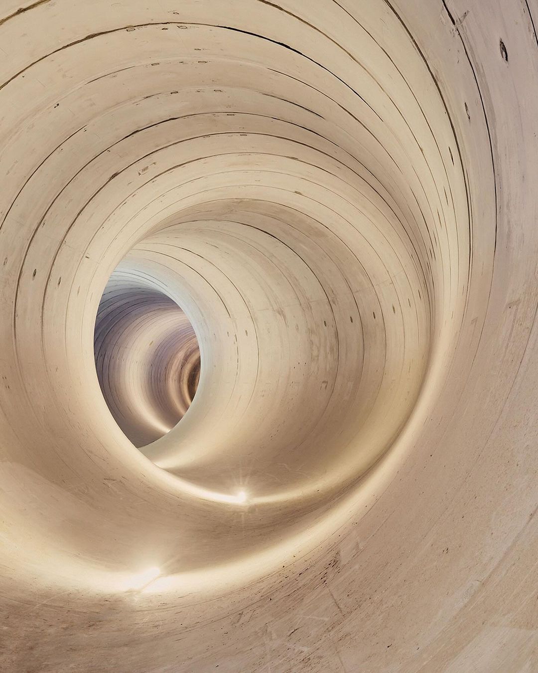 Abstract image of an illuminated tunnel with a textured surface and concentric circles receding into the distance, creating a vortex effect.