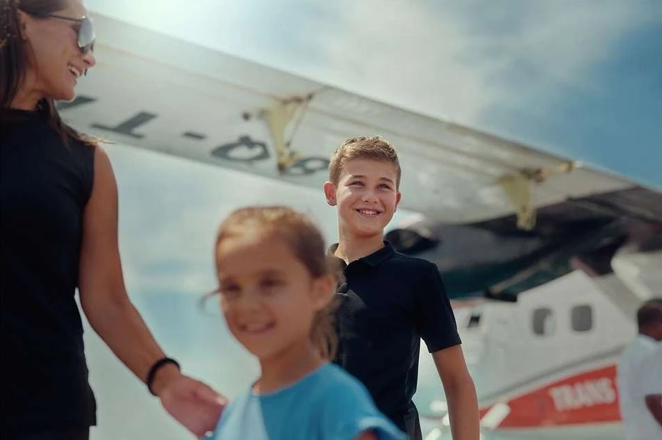 Smiling family—mother, son, and daughter—stand near a small airplane, posing in front of the aircraft on a sunny day with a blue sky.