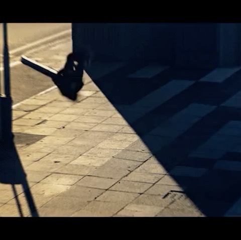 City sidewalk view with a shadowed street lamp creating geometric patterns, casting strong shadows and highlighting textures.