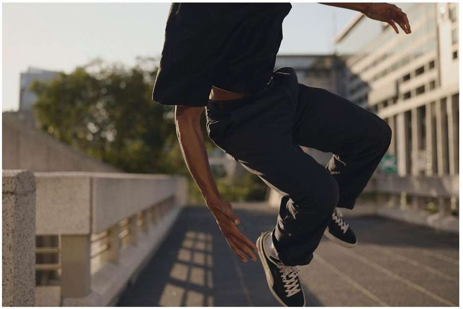 Athletic man in mid-air leaps across a concrete bridge in a black t-shirt, dark pants and sneakers, urban setting, daylight.