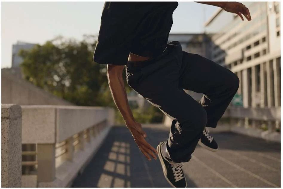 Athletic man in mid-air leaps across a concrete bridge in a black t-shirt, dark pants and sneakers, urban setting, daylight.