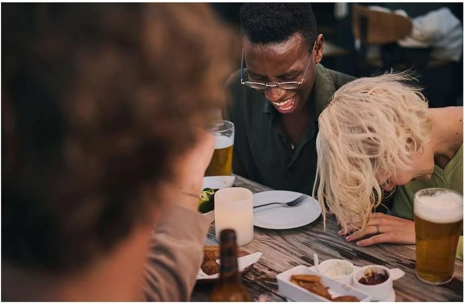 A group of friends at a casual get-together, laughing over drinks and appetizers. Candid moment with an African American male and Caucasian female.