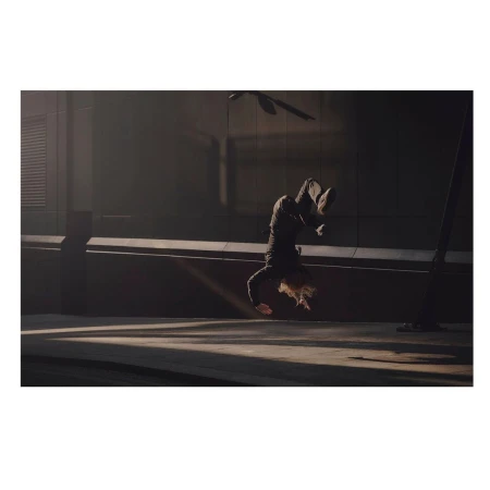 Person in black clothing performing a handstand on a concrete surface with dramatic lighting and architectural backdrop, showcasing fitness and urban style.