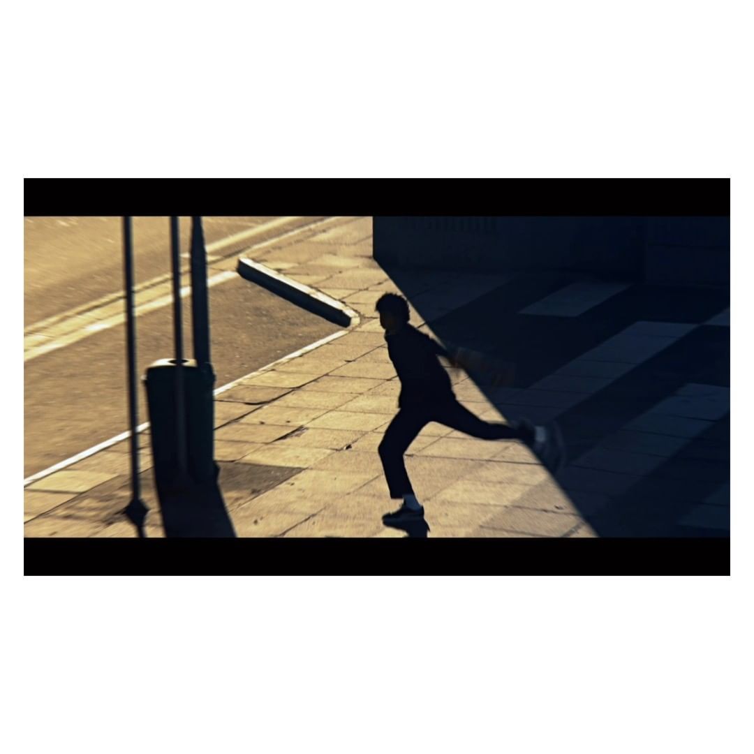 A man in silhouette runs across a sunlit city sidewalk alongside a street, casting a long shadow, creating a sense of movement and urban energy.