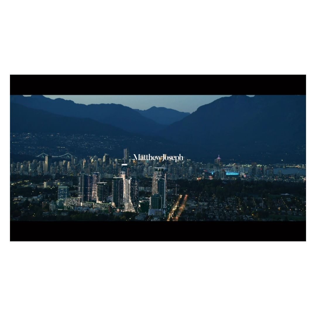 Night cityscape view featuring modern architecture and distant mountains under a dark sky with visible city lights.