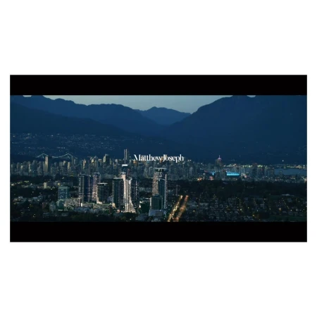 Night cityscape view featuring modern architecture and distant mountains under a dark sky with visible city lights.